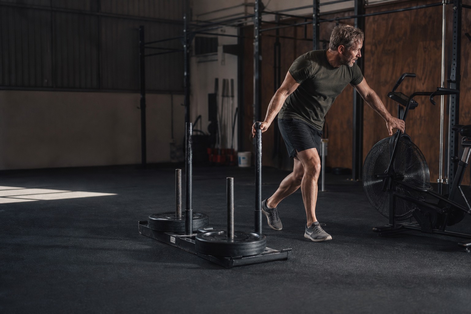 A hybrid athlete transitioning from a weighted sled to an air bike
